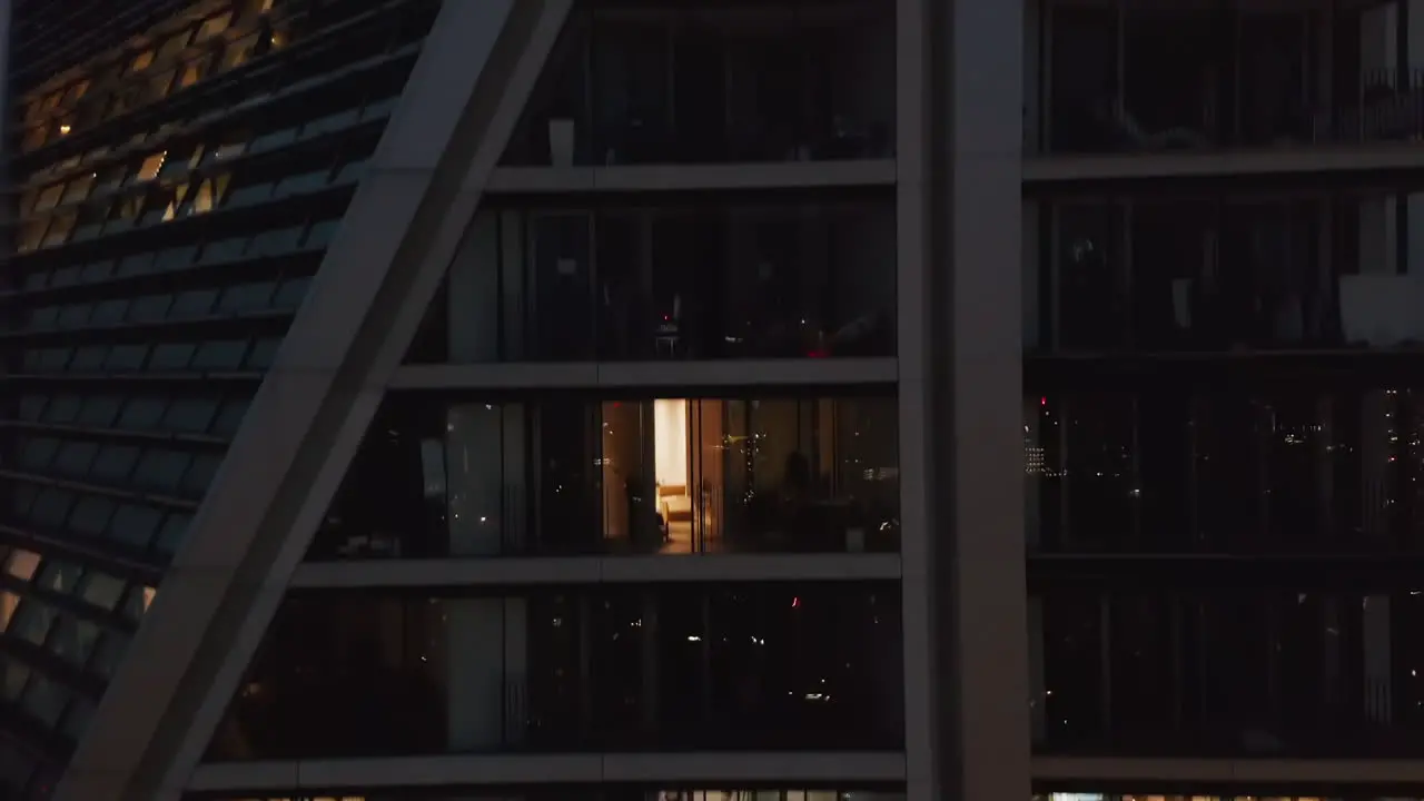 Night view apartment building exterior Ascending footage of glowing windows Revealing cityscape London UK