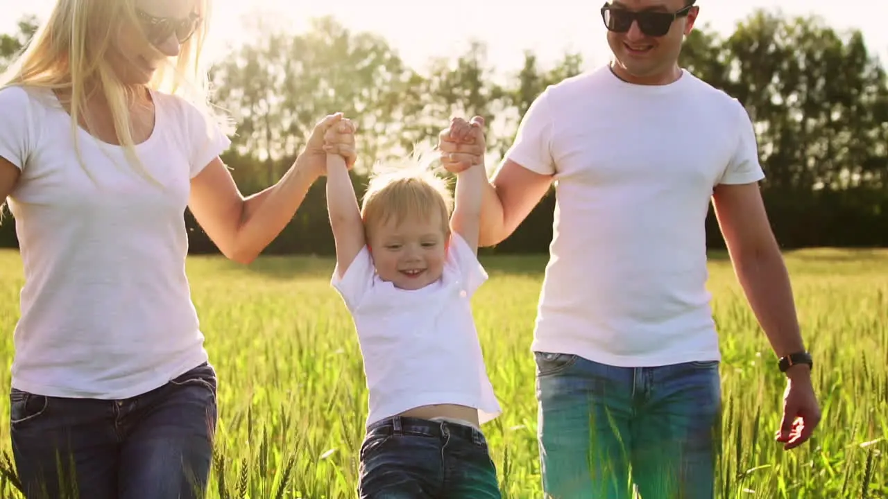 A young family with a young child running in a field with spikelets of wheat swinging a boy in his arms who laughs and smiles with happiness