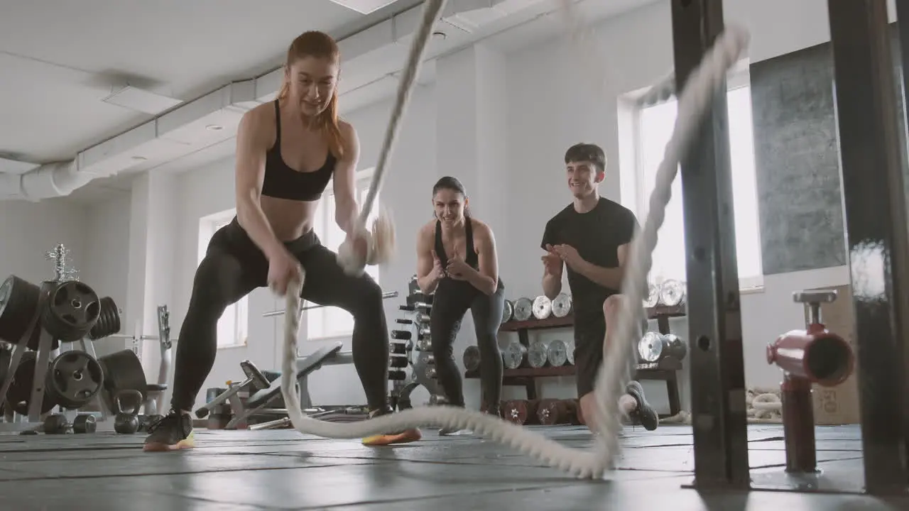 Crossfit Female Bodybuilder Working With Battling Ropes While Gym Buddies Support Her