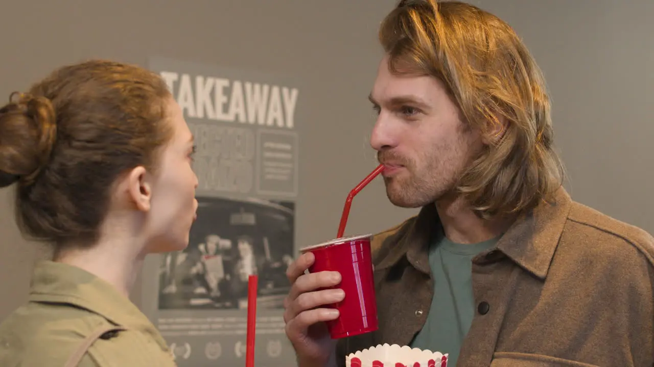 Happy Couple Holding Popcorn Box And Drinking Soft Drink While Talking Together At The Cinema