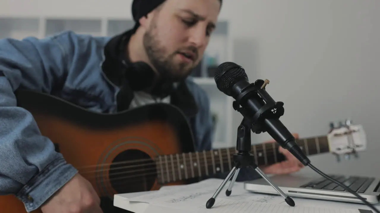 Male Musician Singing And Playing Guitar Recording A Song At Home