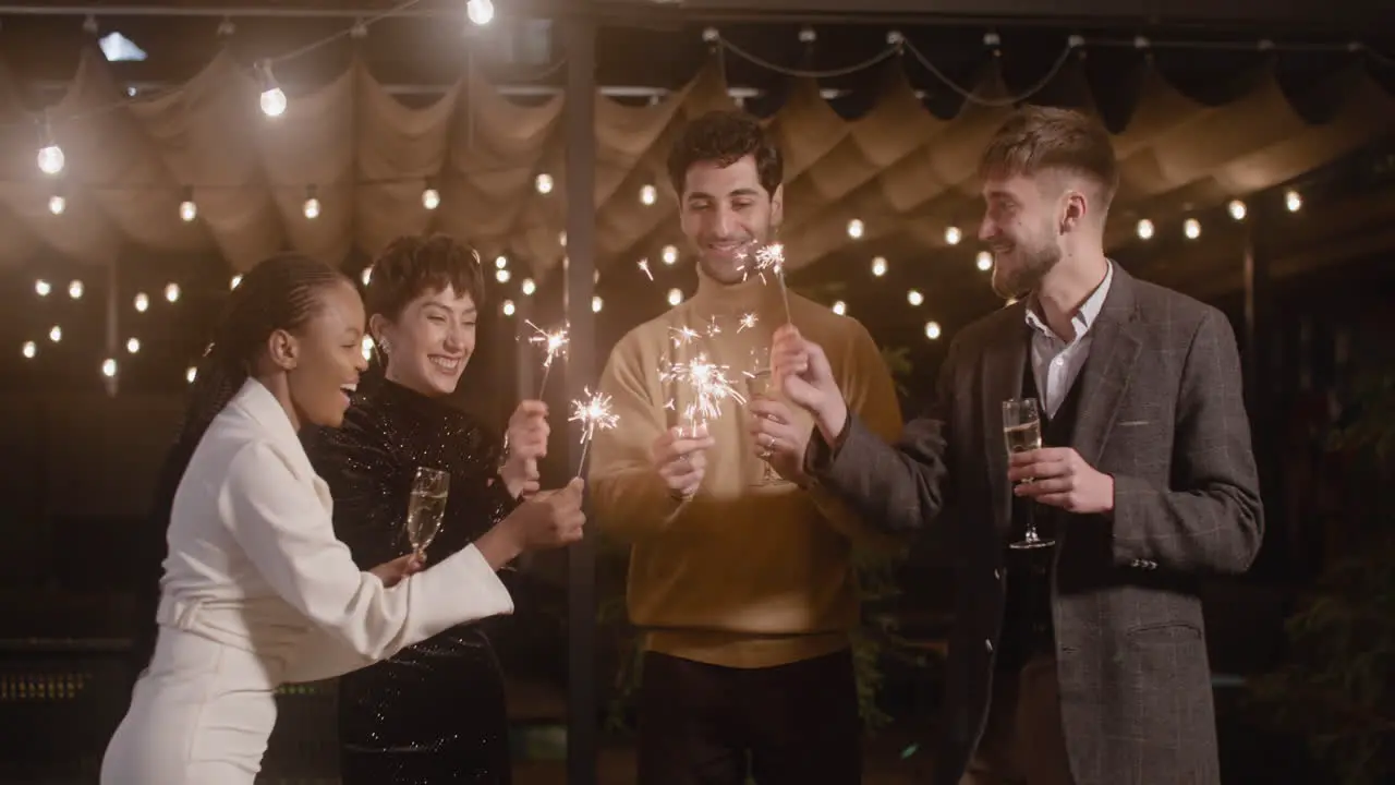 Group Of Four Multiethnic Friends Drinking Champagne And Having Fun With Sparklers At New Year's Eve Party