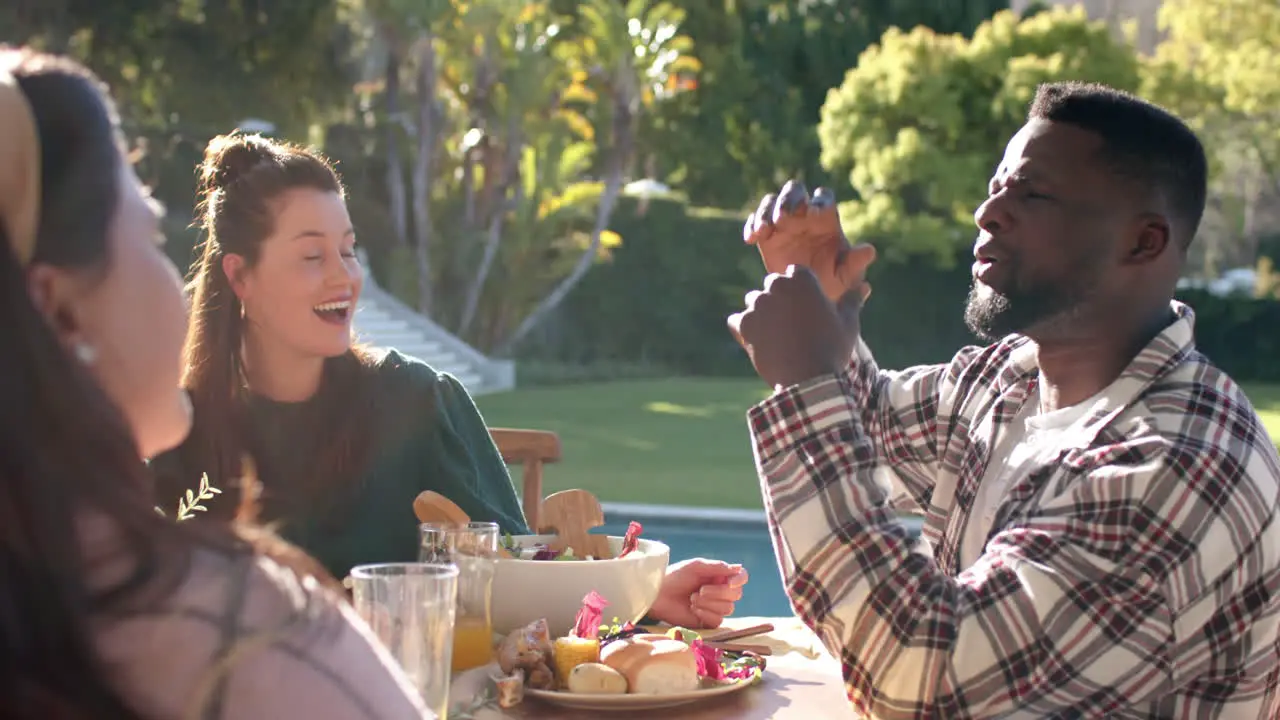 Happy diverse male and female friends talking during thanksgiving celebration meal in sunny garden