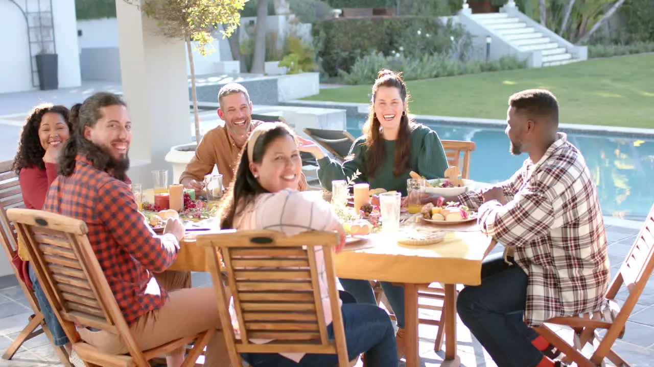 Happy diverse male and female friends enjoying thanksgiving celebration meal in sunny garden