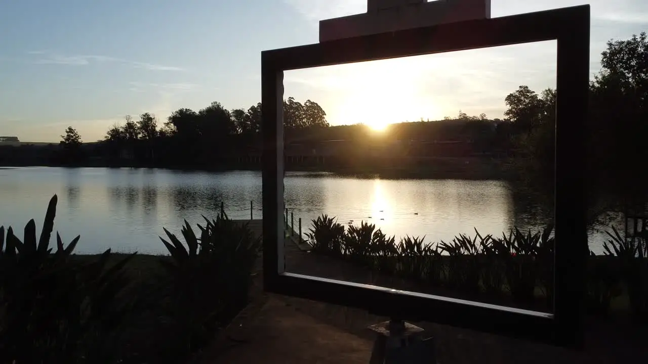 Beautiful shot with drone at sunset passing inside a painting frame with lake and ducks swimming