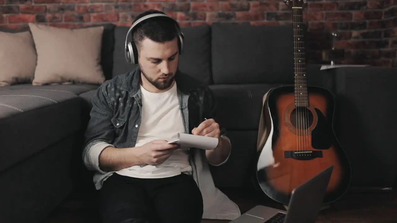 Young Musician Man Listening To Music With Laptop And Wireless Headphones Taking Notes At Home