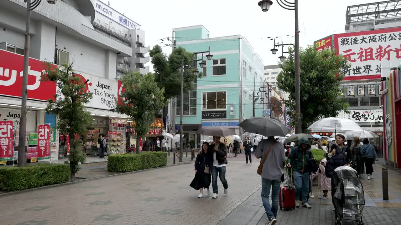 Shoppers Holding Umbrellas Near Tax Free Shops Beside Tsūtenkaku Tower On Overcast Day