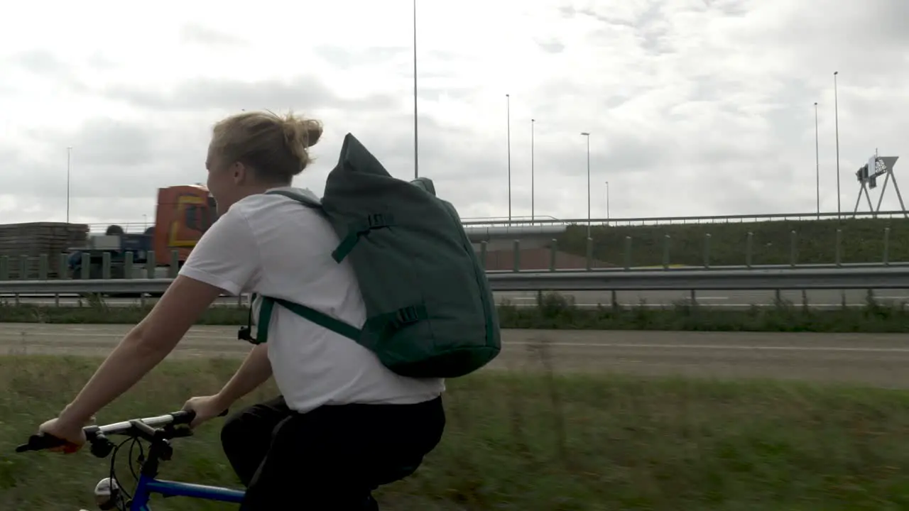 A Young Woman Cycling Near a Main Road in an Urban Area