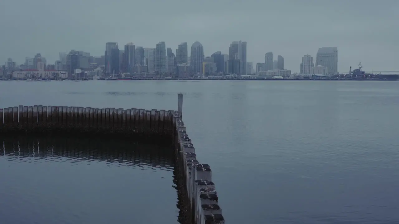 Clip starts out on wooden poles in water then camera tilts up to reveal skyline of San Diego with beautiful reflections in the water