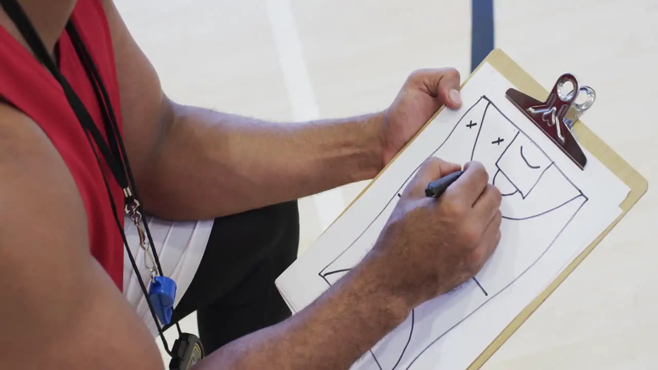 Male african american basketball coach using notebook in indoor court in slow motion