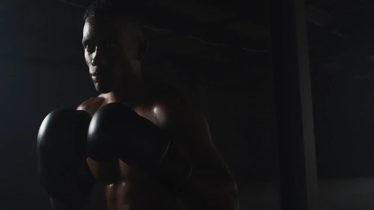 African american man wearing boxing gloves banging fists together in dark room