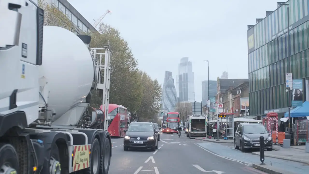 Cars and buses driving down London Whitechapel road with city centre in background tight