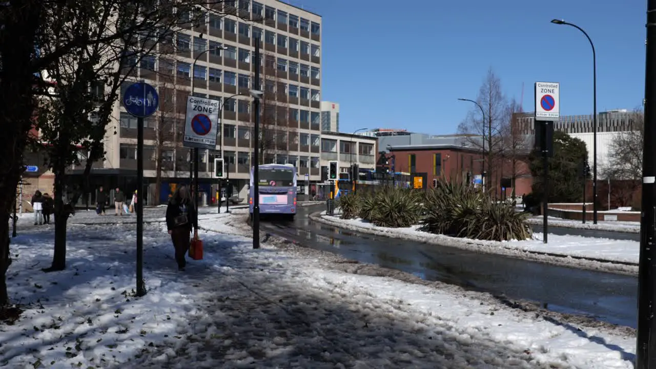 Bus driving through snowy sunny street and woman walking Sheffield