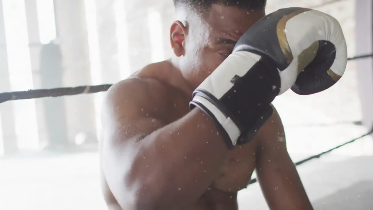 Animation of white particles falling over african american male boxer resting after training