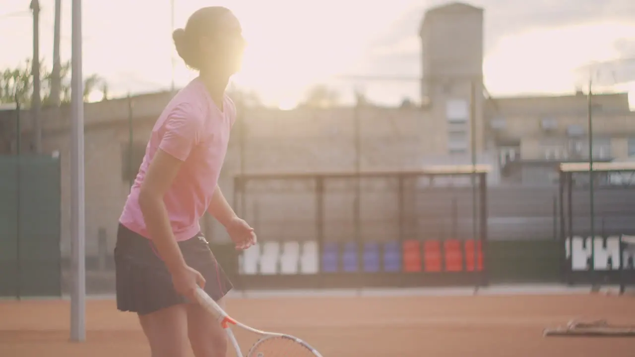 A female tennis player on the court hits a ball in the sun in slow motion