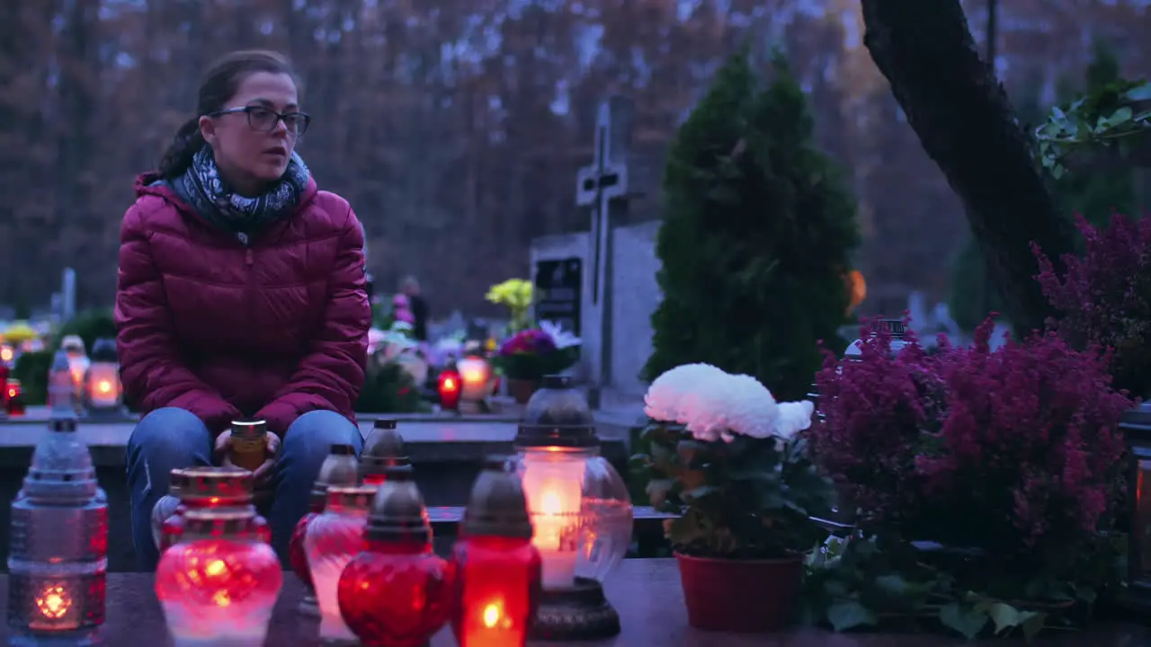 Woman in grief at a grave lit by burning grave candles