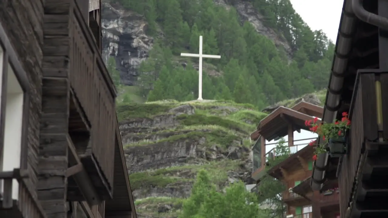 Tilt up shot of small town in Zermatt and showing big white cross on hill top