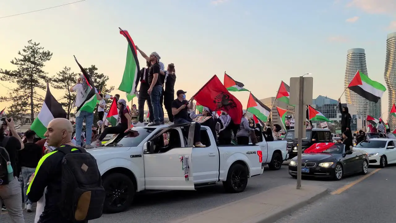 Free Palestine protesters rally standing on cars waving Palestine flags and chanting support during Israel conflict