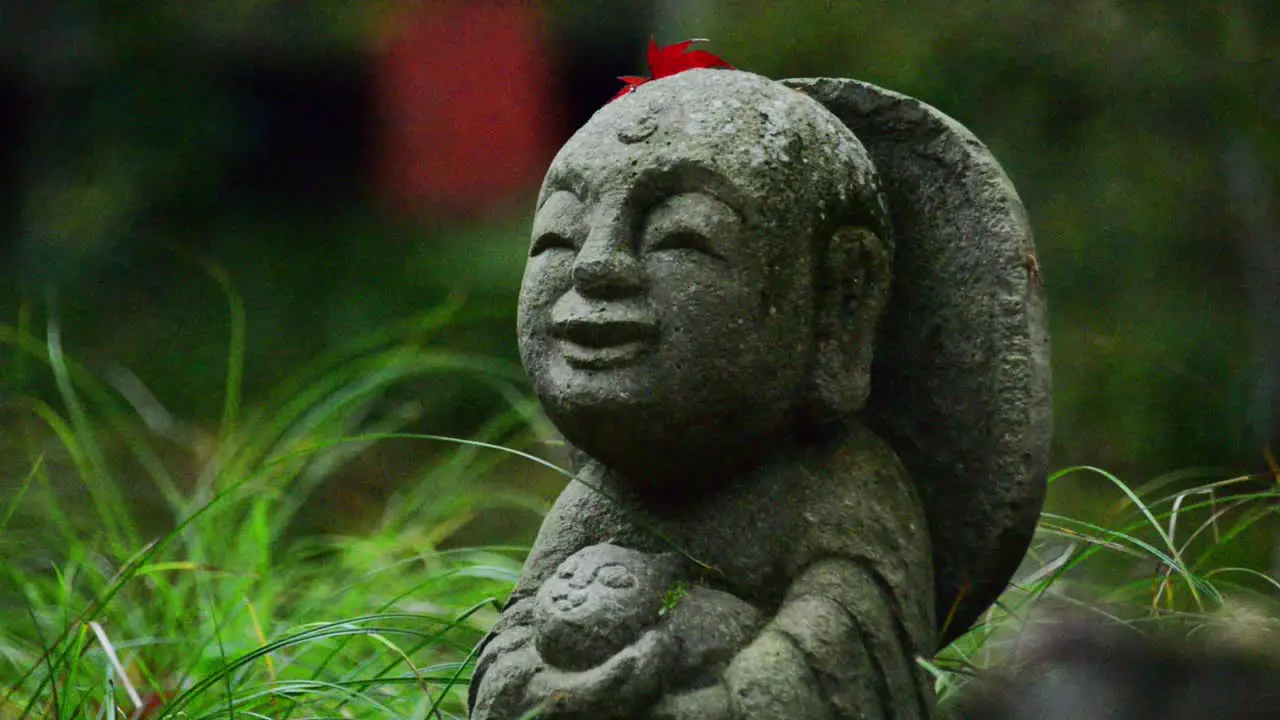 A small Jizo staute with a red leaf on its head staying in lush green grass