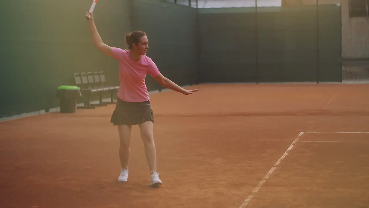 Young woman walking through tennis court with racket Backside view of attractive brunette female in blue shirt and black shorts entering tennis hardcourt Full length follow shot with copy space