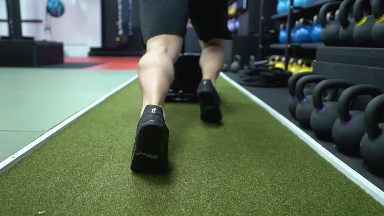 A strong man is pushing a prowler sled in the gym on the green turf floor