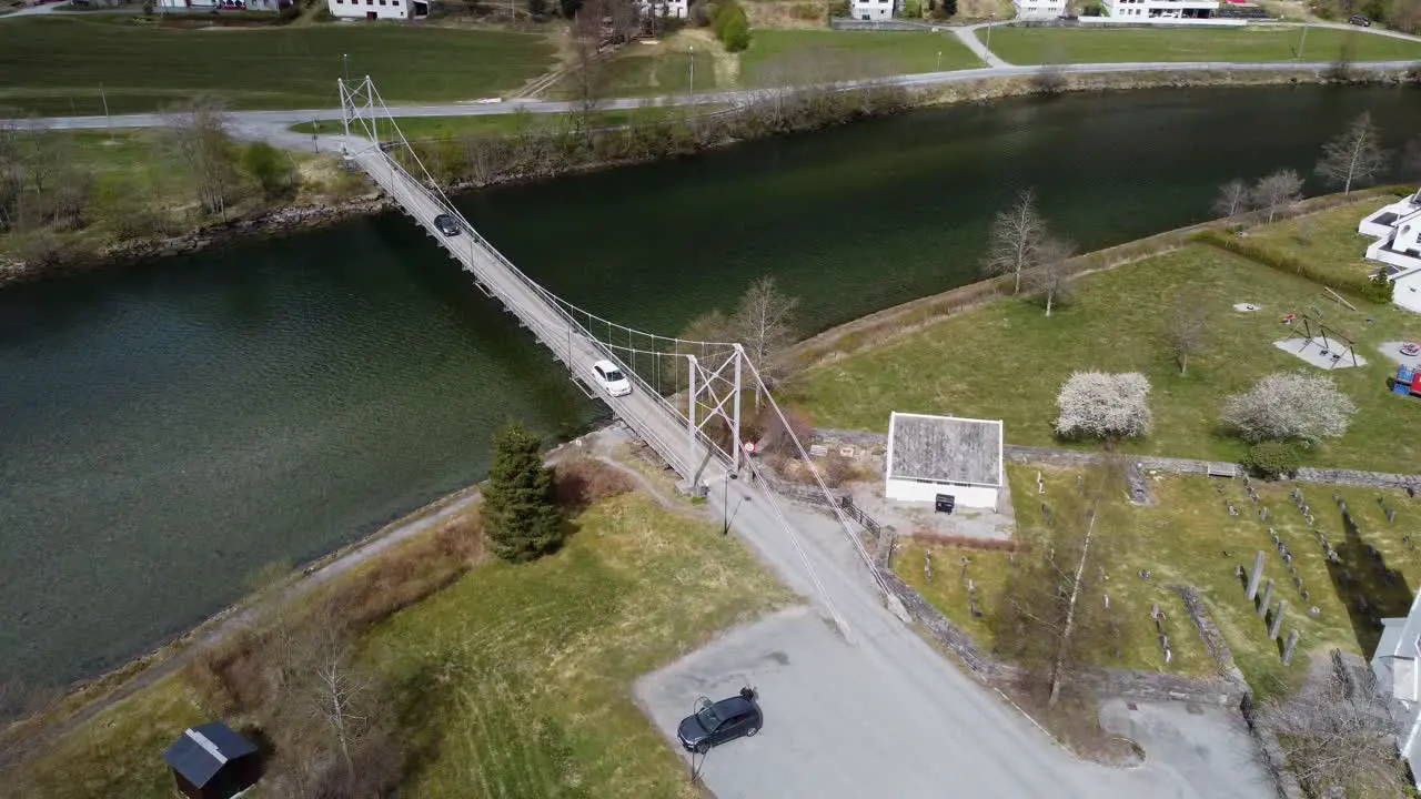 Two cars crossing over Modalen river on old suspension bridge Aerial Modalen Norway with church