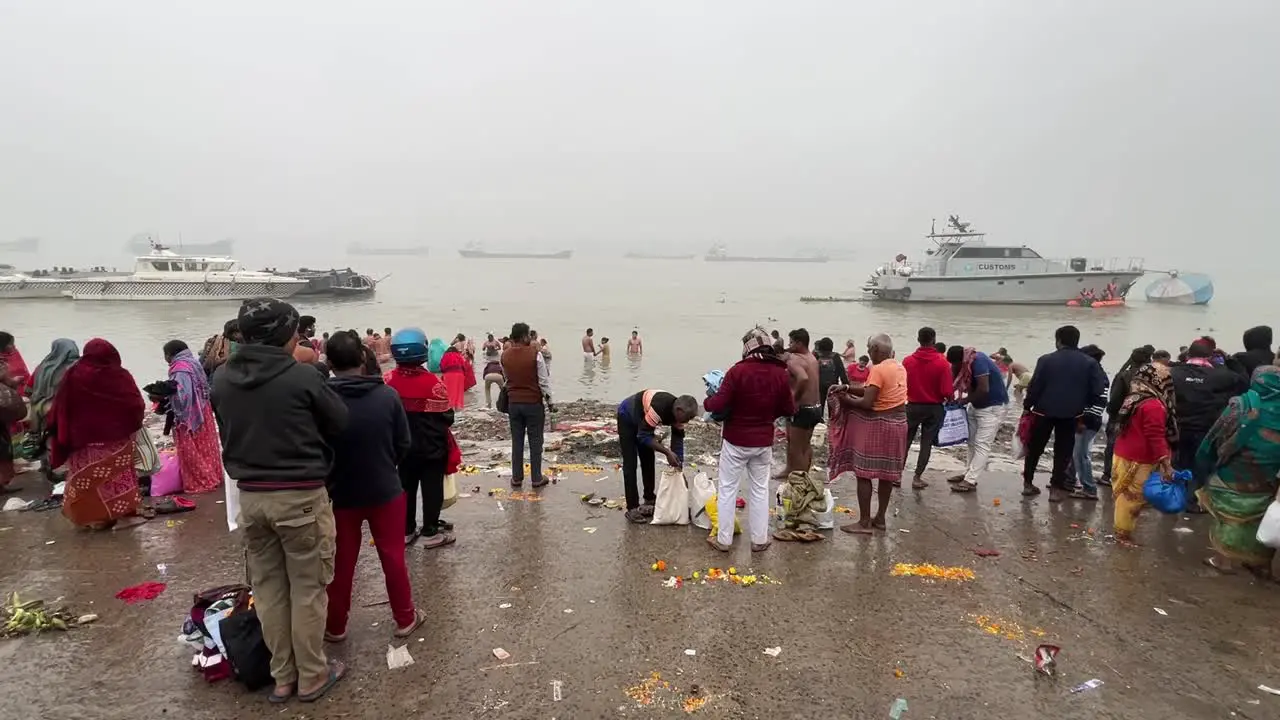 Wide angle static shot of People bathing and praying during Sankranti near a jetty in Babughat Kolkata during foggy evening