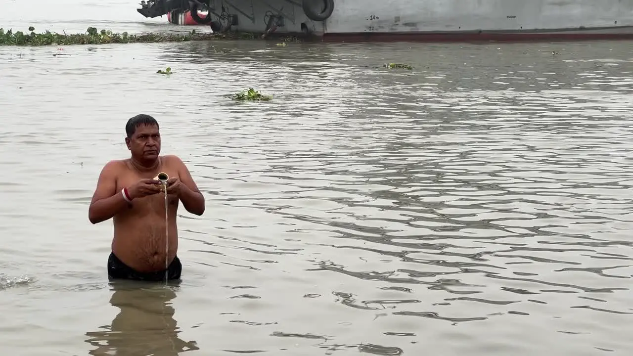 Profile view of a man talking the holy dip and praying in foggy winter morning during Sankranti with jetty in the background in Babughat Kolkata