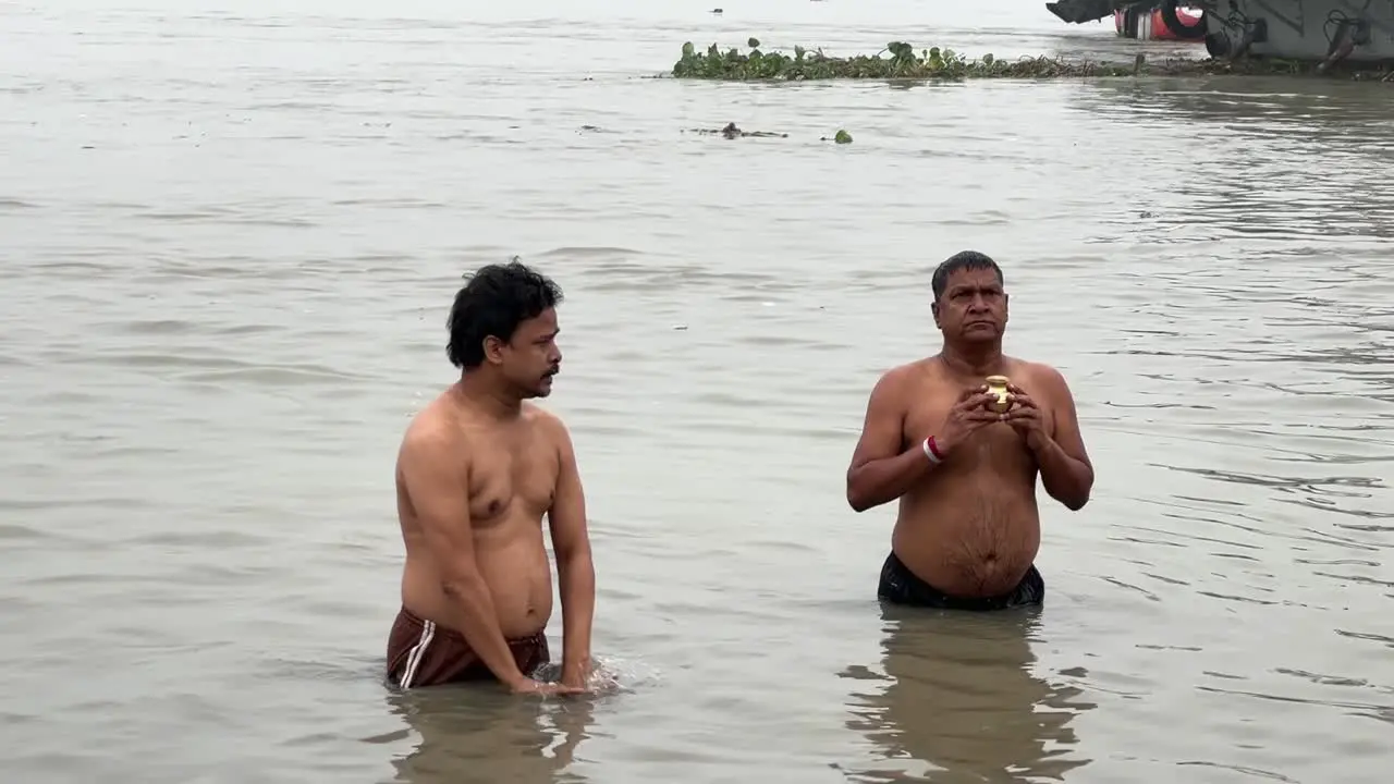 Static shot of men talking the holy dip and praying in foggy winter morning during Sankranti with seascape in the background