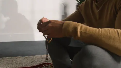 Close Up Of Muslim Man Praying Holding Prayer Beads Casting Shadow On Wall Behind 2