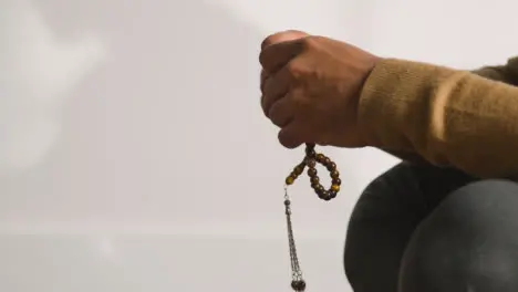 Close Up Of Muslim Man Praying Holding Prayer Beads Casting Shadow On Wall Behind