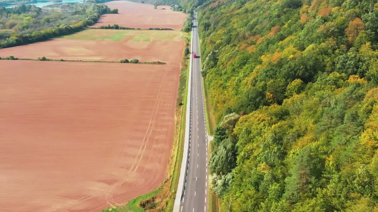 There is a road in the middle of the shot on one side of the road is a big forest on the other side there is brown ground