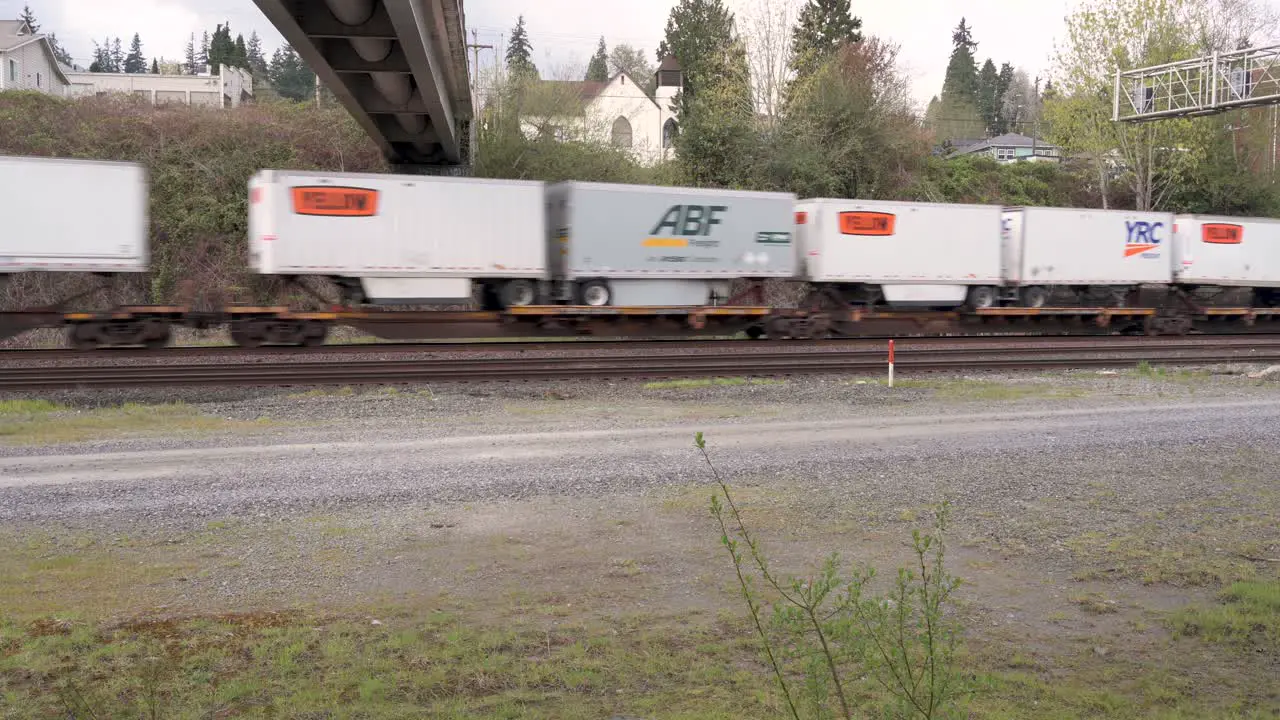 Train of flatbed cars carrying truck containers travels beneath underpass