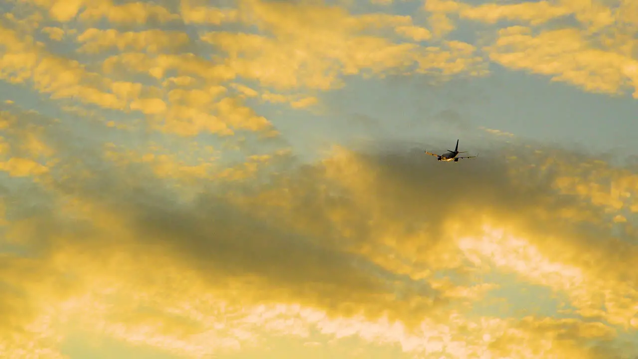 Jet Airplane Flying Off Into Distance Against Golden Hour Sunset Light Being Reflected Off Clouds