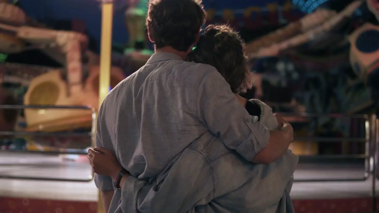 The Loving Couple Is Standing And Looking At The Luminous Attraction At The Amusement Fair