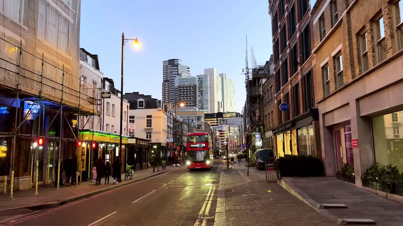 Red London bus driving through streets of Shoreditch with skyscrapers