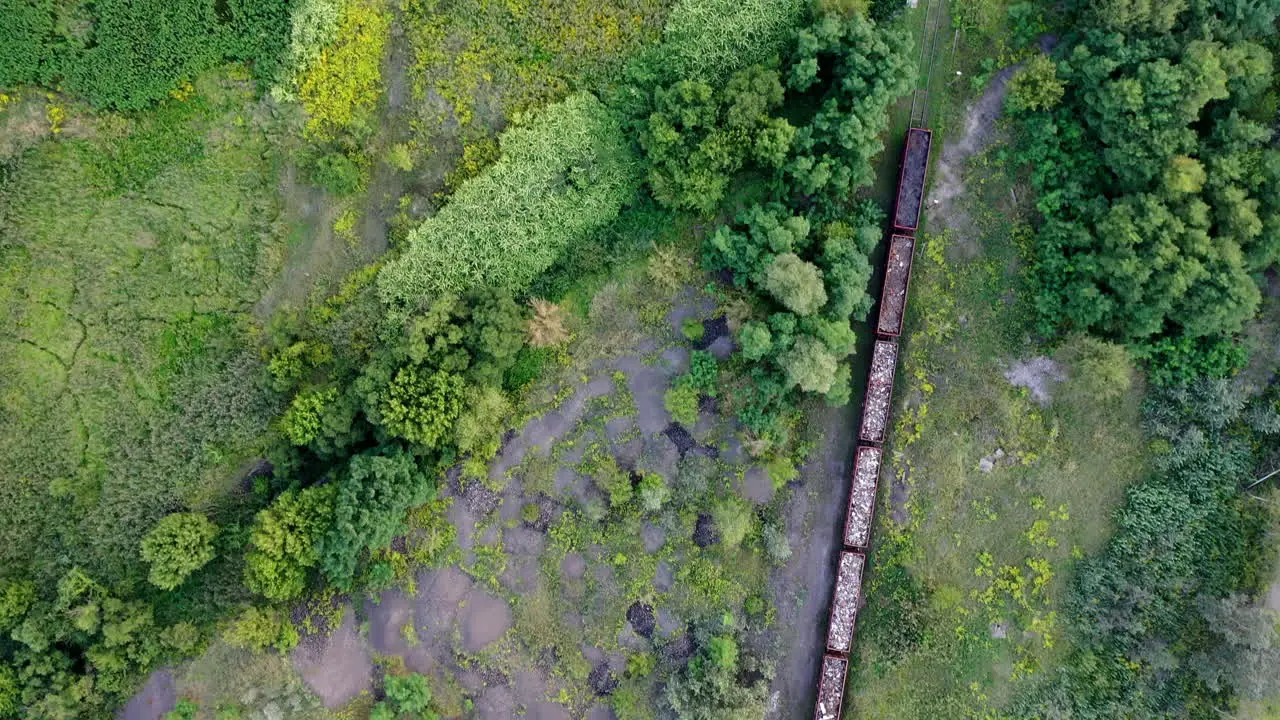 Drone shot flying over a cargo train riding the track through nature