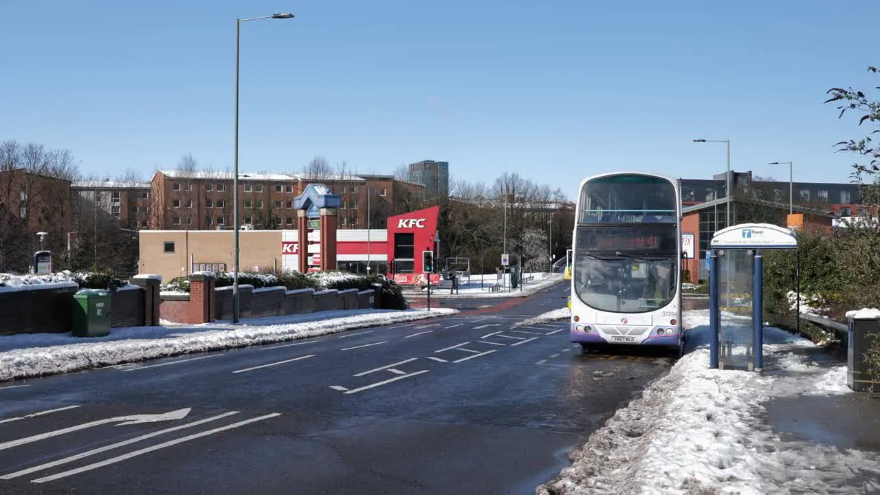 Bus leaving bus stop and traffic driving past on sunny snowy road Sheffield