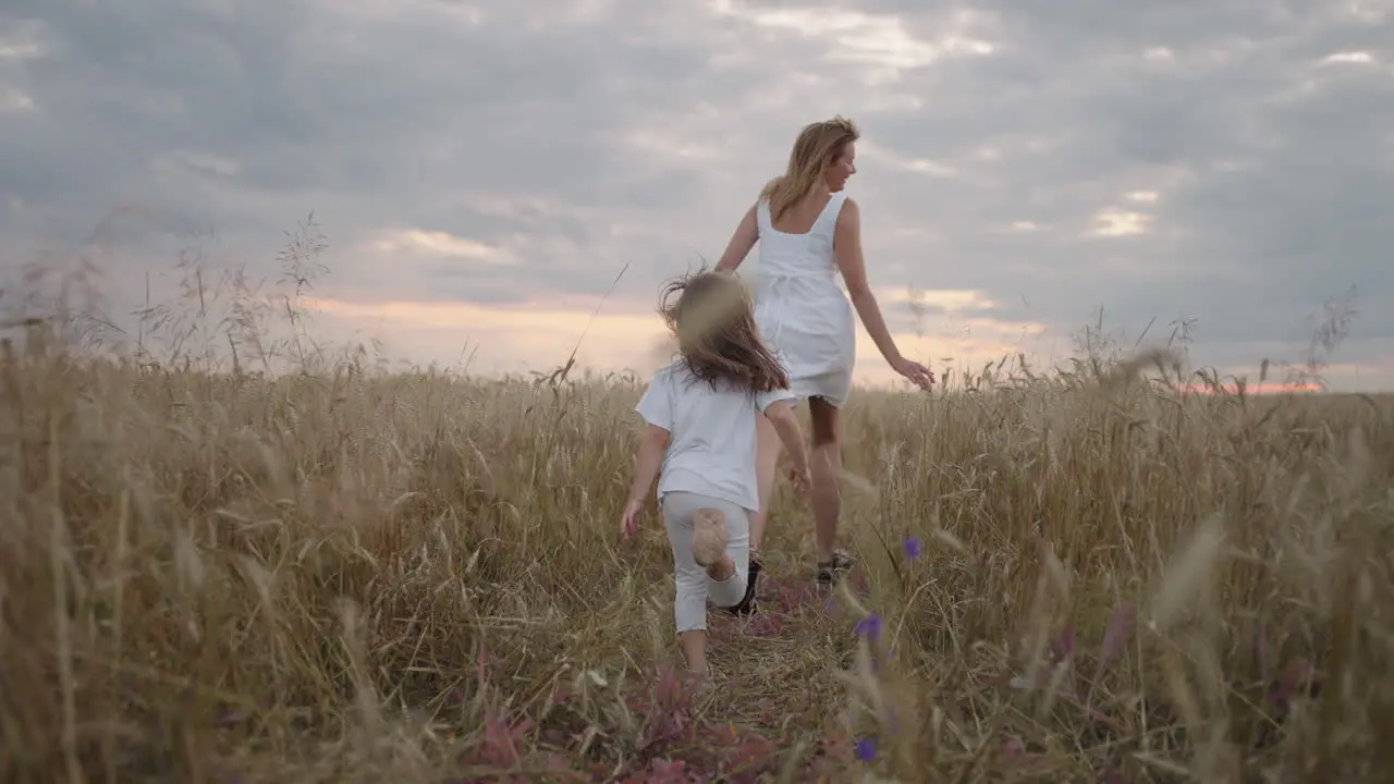 Daughter and mother dream together run in the wheat field at sunset happy family people in the wheat field concept Mom and girl playing catch-up run baby child fun running in green meadow