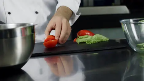 Chef cooking fresh salad at kitchen Closeup chef hands cutting tomato