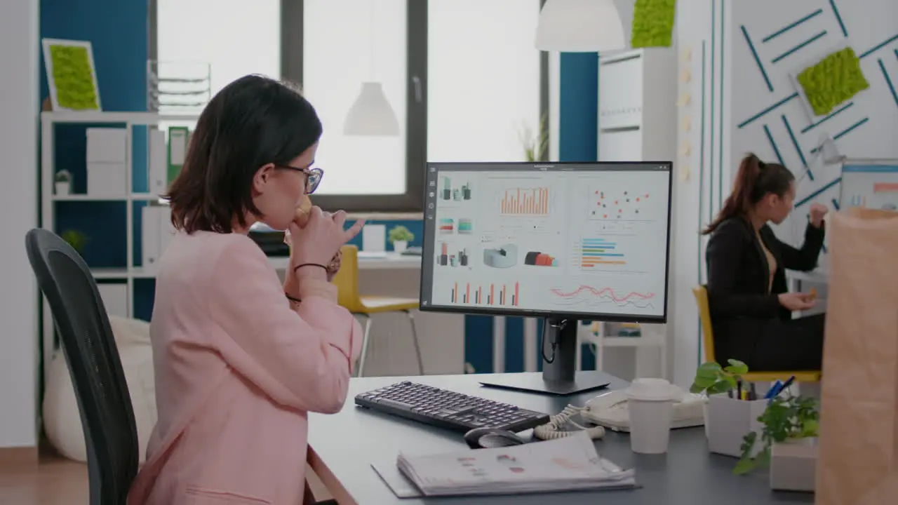 Executive manager eating tasty sandwich while analyzing marketing strategy at desk