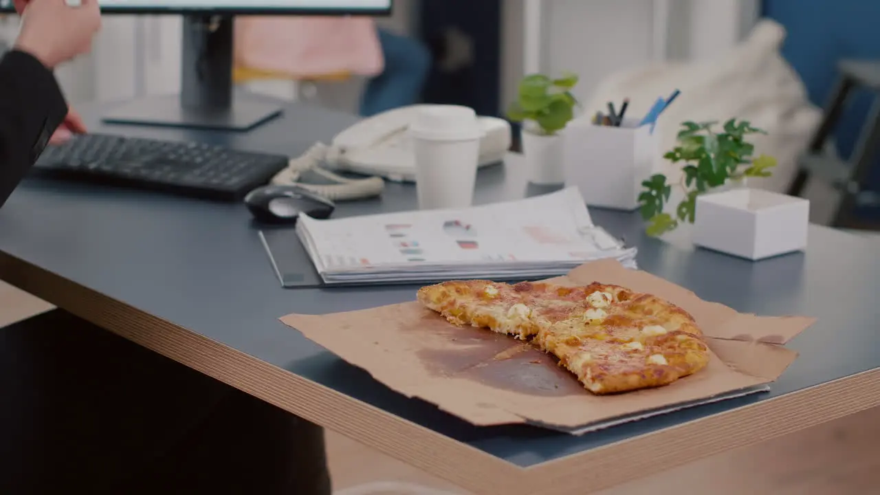 Closeup of executive manager taking slice of pizza eating in front of computer typing financial graphs