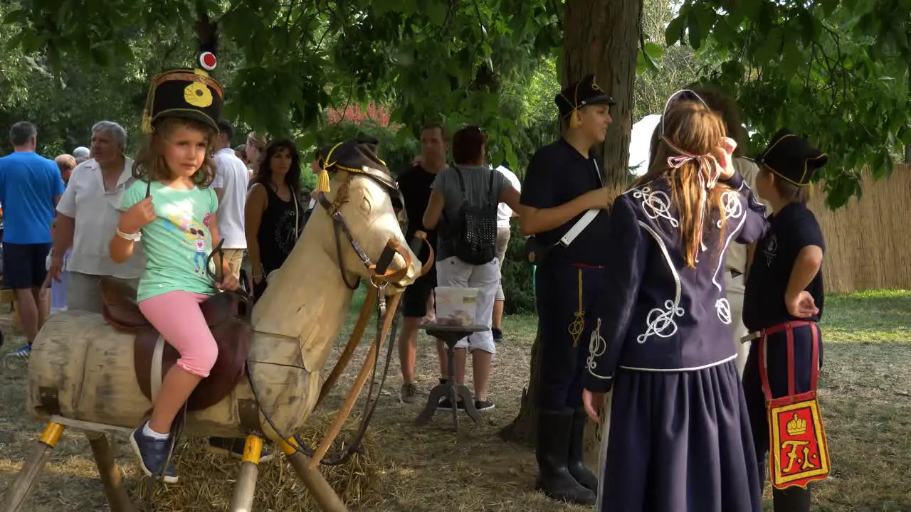 Savaria carnival hussar boy teaching a girl to ride wooden horse talking with civilian