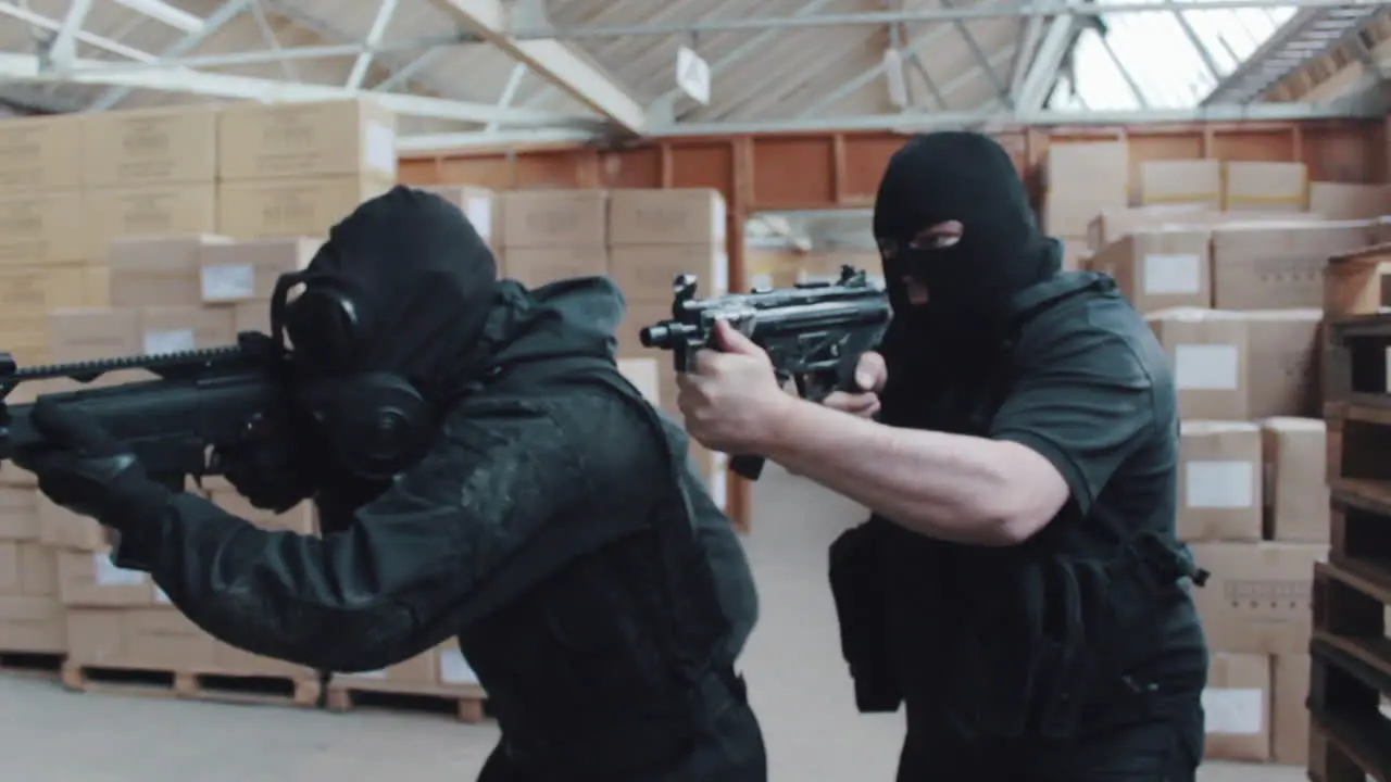 A police swat team searches a warehouse with guns drawn wearing balaclavas an gas masks