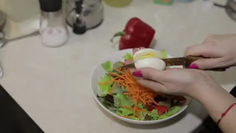 Female hands cut an egg to a salad with red bell Pepper and lettuce salad