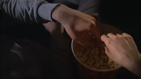 Female and male hand take popcorn grains from popcorn box in slow motion