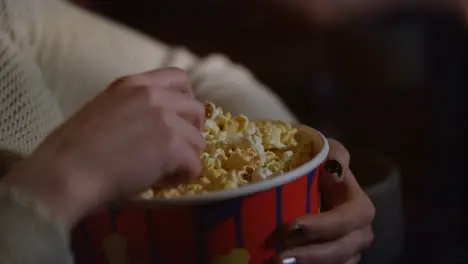 Female hand taking popcorn from paper container Eating pop corn at cinema