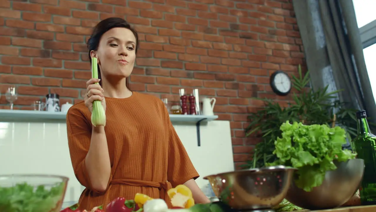 Woman tasting fresh celery in kitchen Joyful brunette cooking healthy food