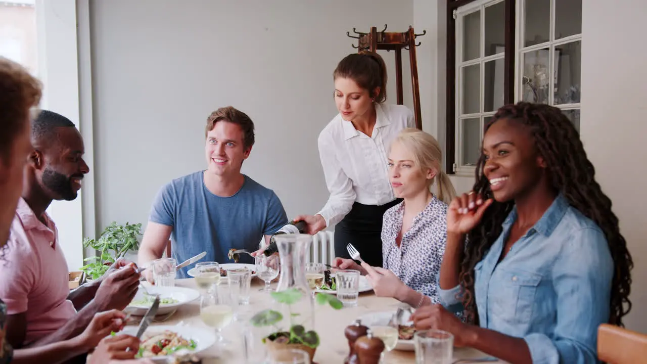 Waitress Serving Wine To Group Of Friends Eating Meal In Restaurant Together