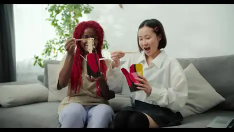 Diverse female friends eating together at home using chopsticks